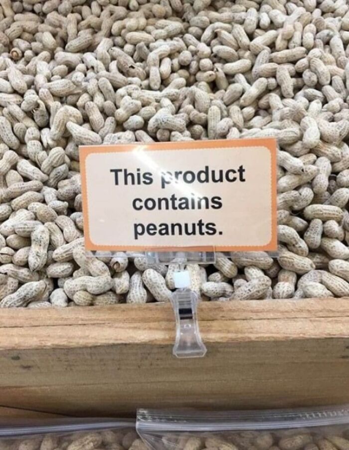 Sign stating "This product contains peanuts" placed on a pile of peanuts, highlighting warning signs and errors. Sign stating "This product contains peanuts" placed on a pile of peanuts, highlighting warning signs and errors.